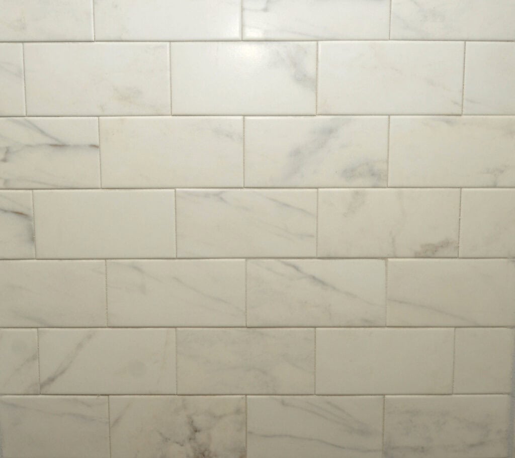 White rectangular marble tiles with subtle gray veining arranged in a horizontal subway pattern on a wall.