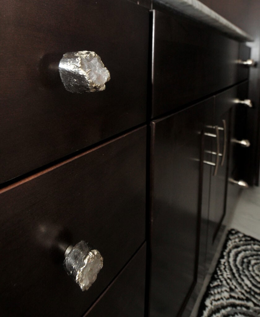 Close-up of dark wood cabinets with unique, rough crystal drawer pulls featuring metallic accents, and a patterned black and white rug partially visible on the floor.
