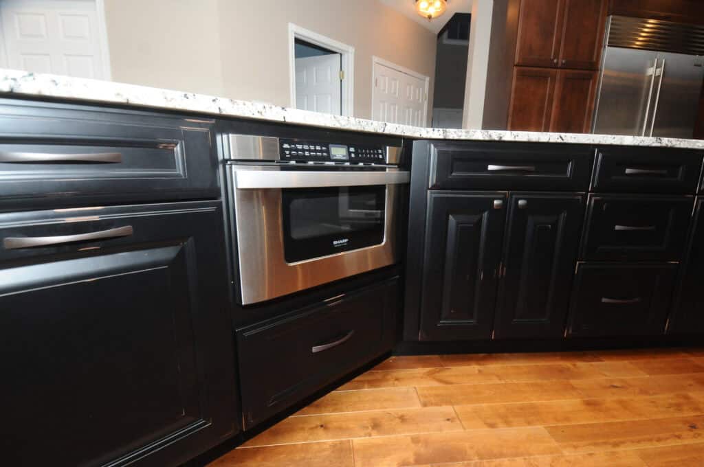A modern kitchen features dark cabinets, a built-in stainless steel microwave, granite countertops, and wood flooring. White doors and walls are visible in the background.