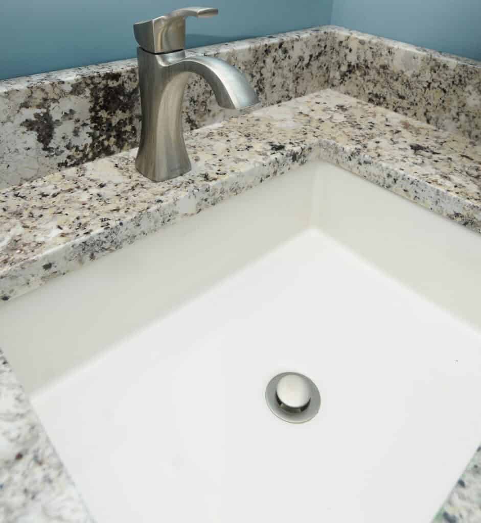 A close-up view of a modern bathroom sink with a rectangular white basin, granite countertop, and a brushed metal faucet against a light blue wall.