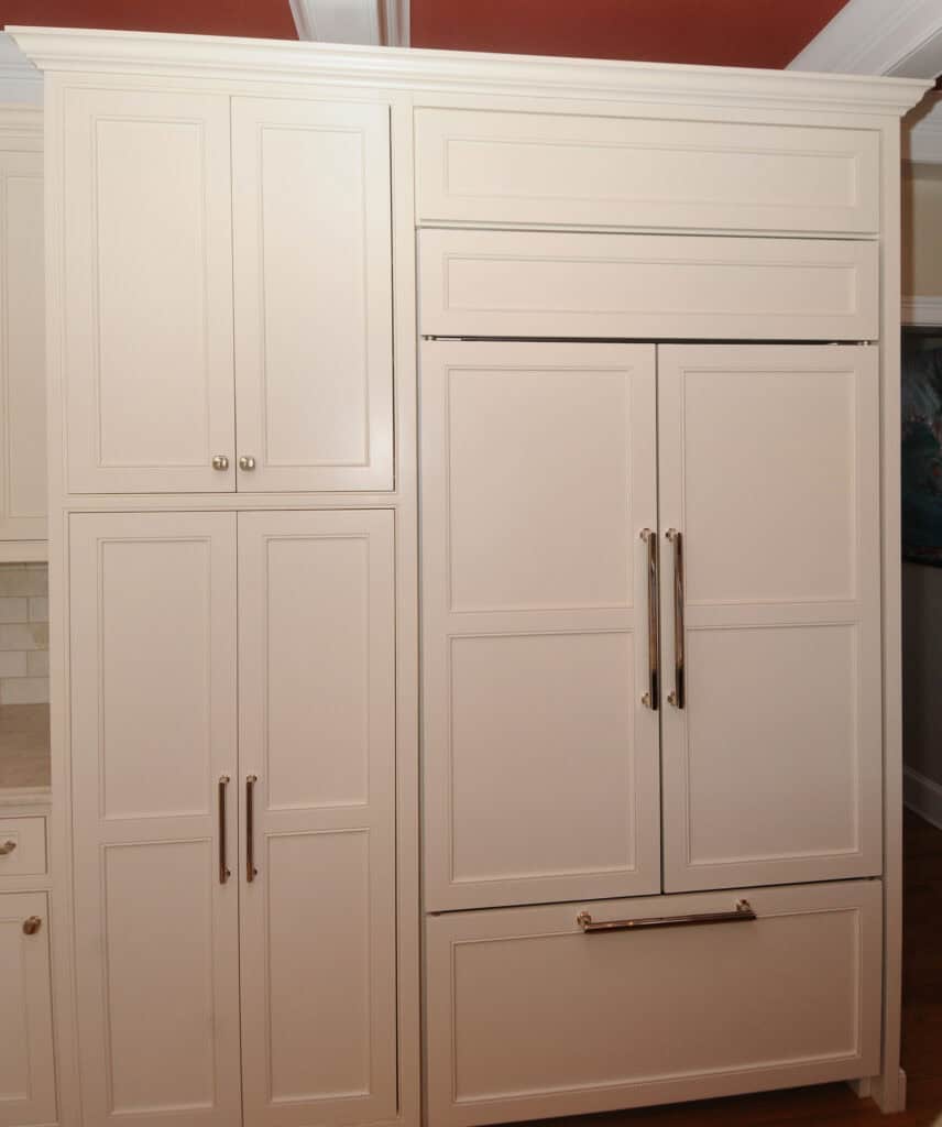 Cream-colored kitchen cabinets and a built-in refrigerator with panel doors that match the cabinetry, all featuring brass handles and a clean, modern design.
