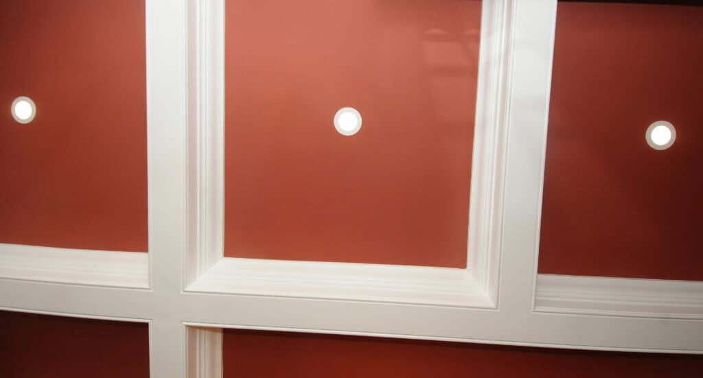 Red ceiling with white grid-like beams and three round recessed lights evenly spaced in the center of the panels.