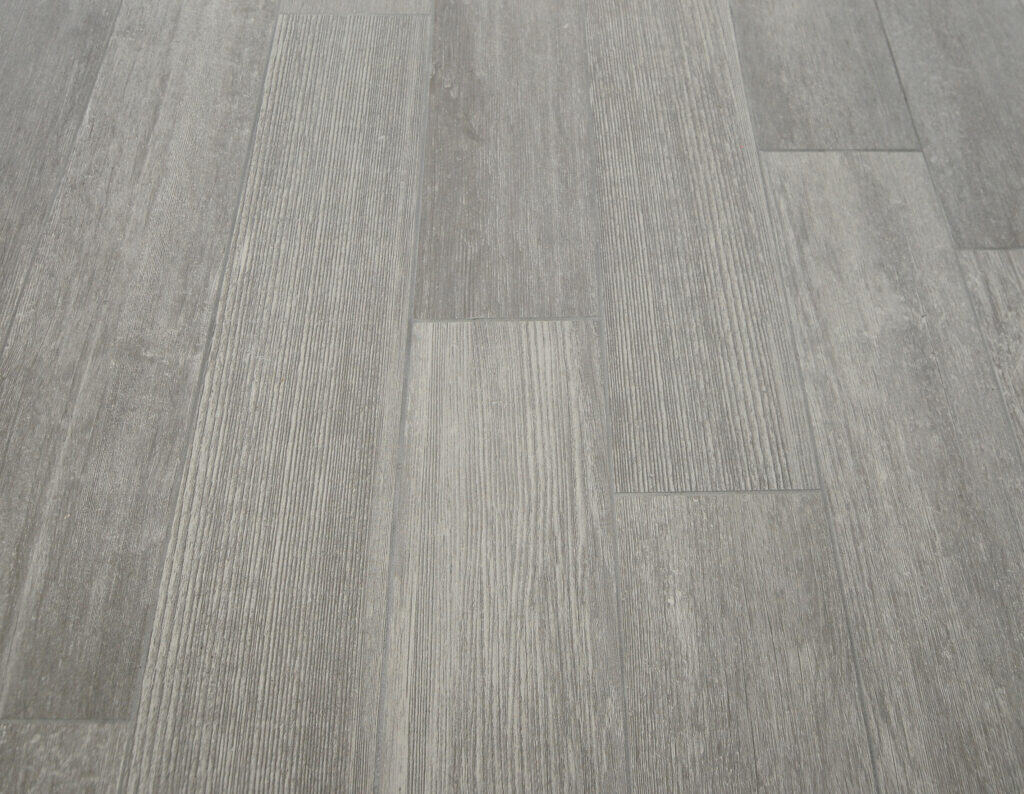 Close-up view of a gray wood-look vinyl floor with textured, rectangular planks arranged in a staggered pattern, showcasing a subtle grain and varying shades of gray.