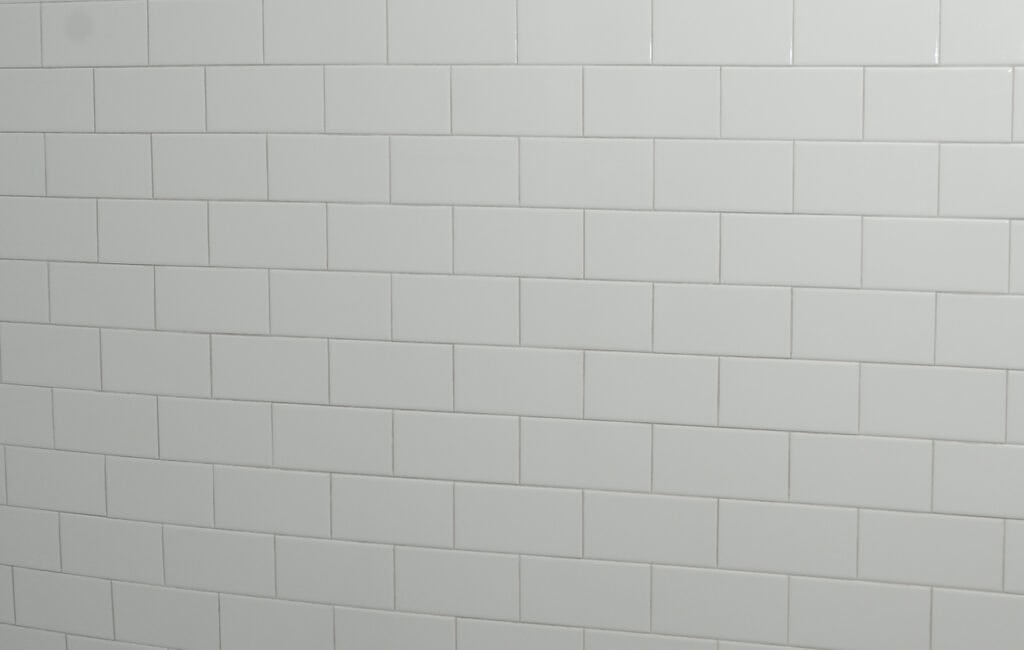 White rectangular subway tiles arranged in a horizontal brick pattern on a wall, with visible grout lines creating a clean and simple appearance.
