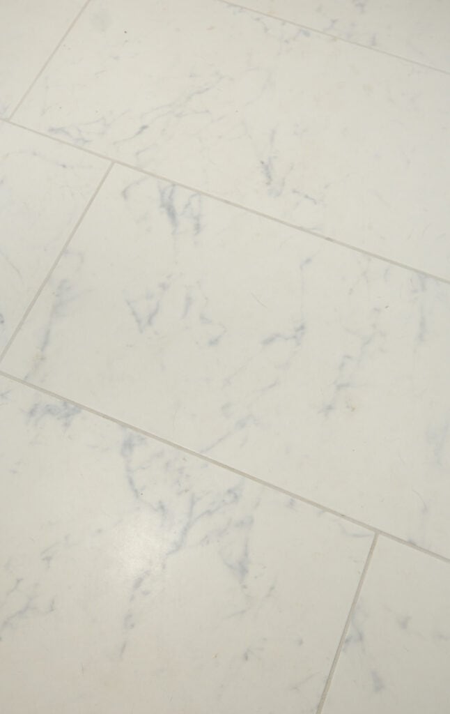 White tiles with subtle gray veining arranged in a staggered pattern, resembling a marble surface. The tiles have a smooth, matte finish and clean grout lines.
