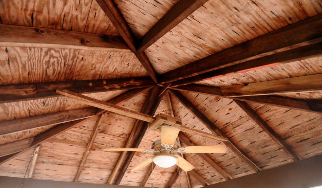 Wooden ceiling with exposed beams arranged in a radial pattern, converging at the center. A ceiling fan with light and wooden blades hangs from the center of the ceiling.