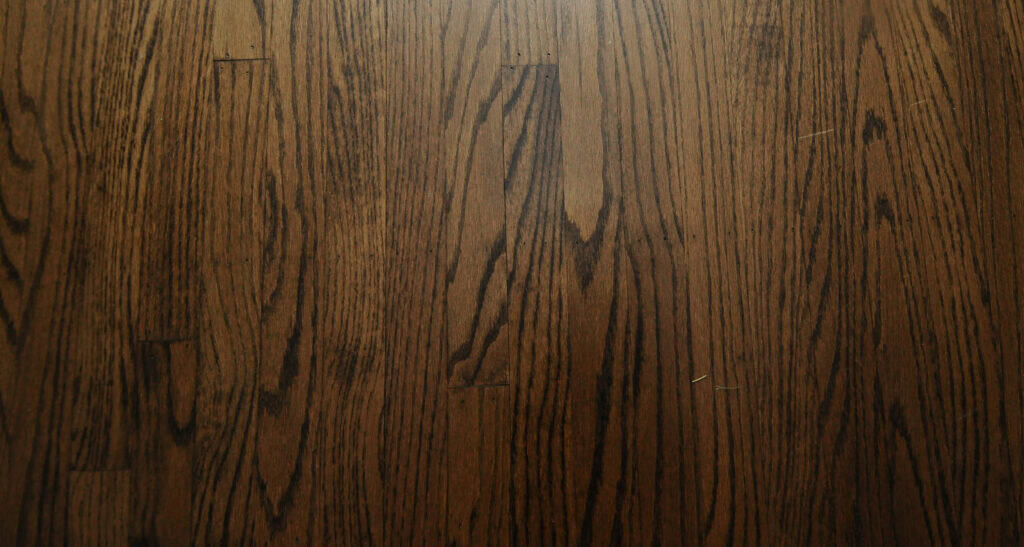Close-up view of a dark brown wooden floor with visible natural grain patterns and a few small scratches and imperfections.