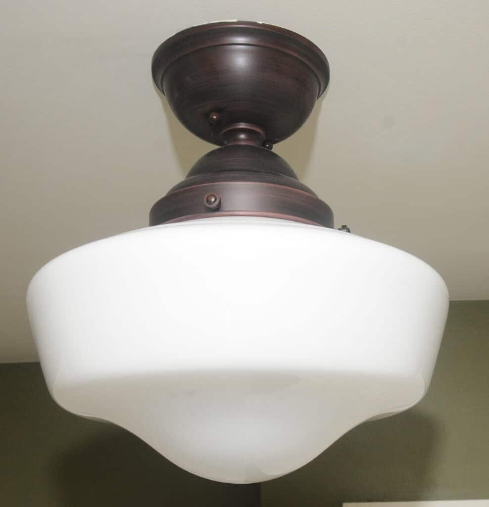 A close-up view of a ceiling-mounted light fixture with a dark metal base and a large, rounded white glass shade.