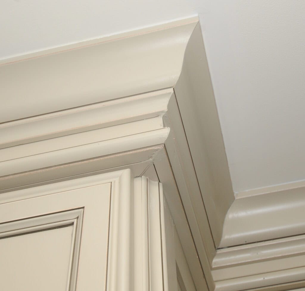 Close-up of an interior corner where cream-colored crown molding meets the ceiling and cabinets, showing detailed woodwork and joints.