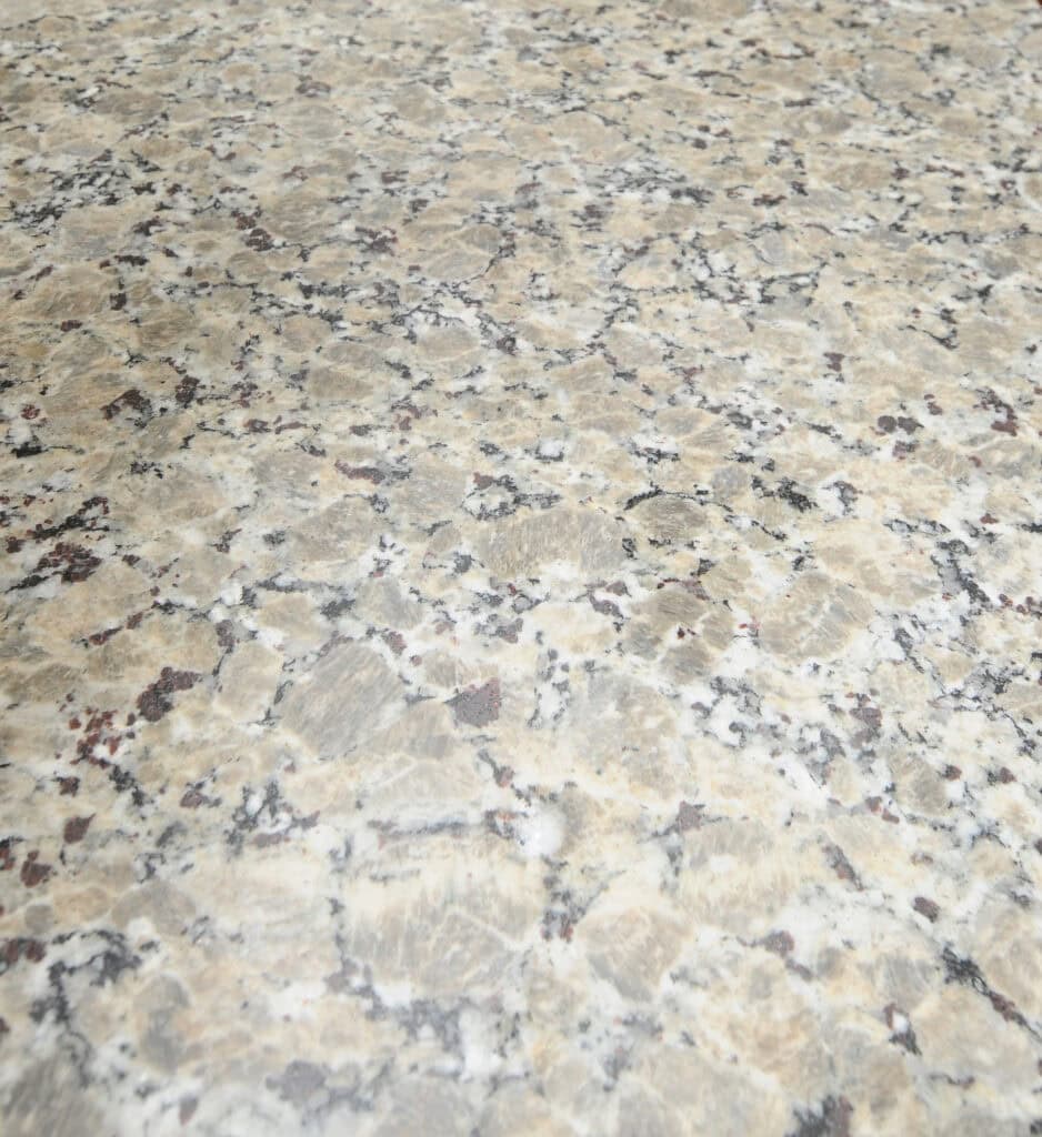 A close-up view of a polished granite countertop featuring a beige background with black, white, and brown speckles and veins throughout the stone surface.
