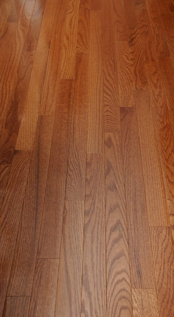 Close-up view of a polished wooden floor with medium brown planks, showing natural wood grain patterns and variations in color.