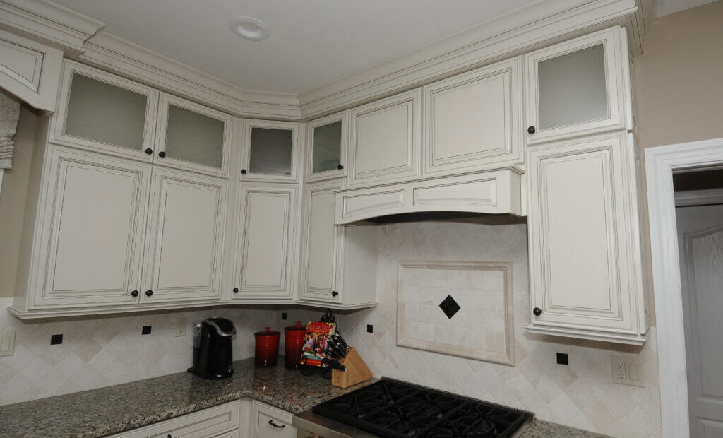 A modern kitchen with white cabinets, granite countertops, a gas cooktop, and a tiled backsplash featuring a small black diamond design. Small appliances and utensils are on the counter.
