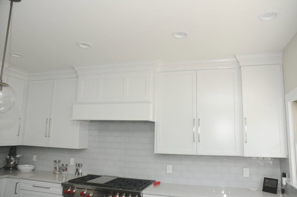 A modern kitchen with white cabinets, stainless steel stove, light gray subway tile backsplash, and a white quartz countertop. Some small appliances and items are on the counter.