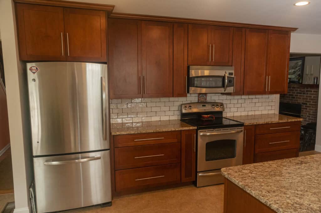 Modern kitchen with wooden cabinets, stainless steel appliances including a refrigerator, oven, and microwave, granite countertops, and a white subway tile backsplash.