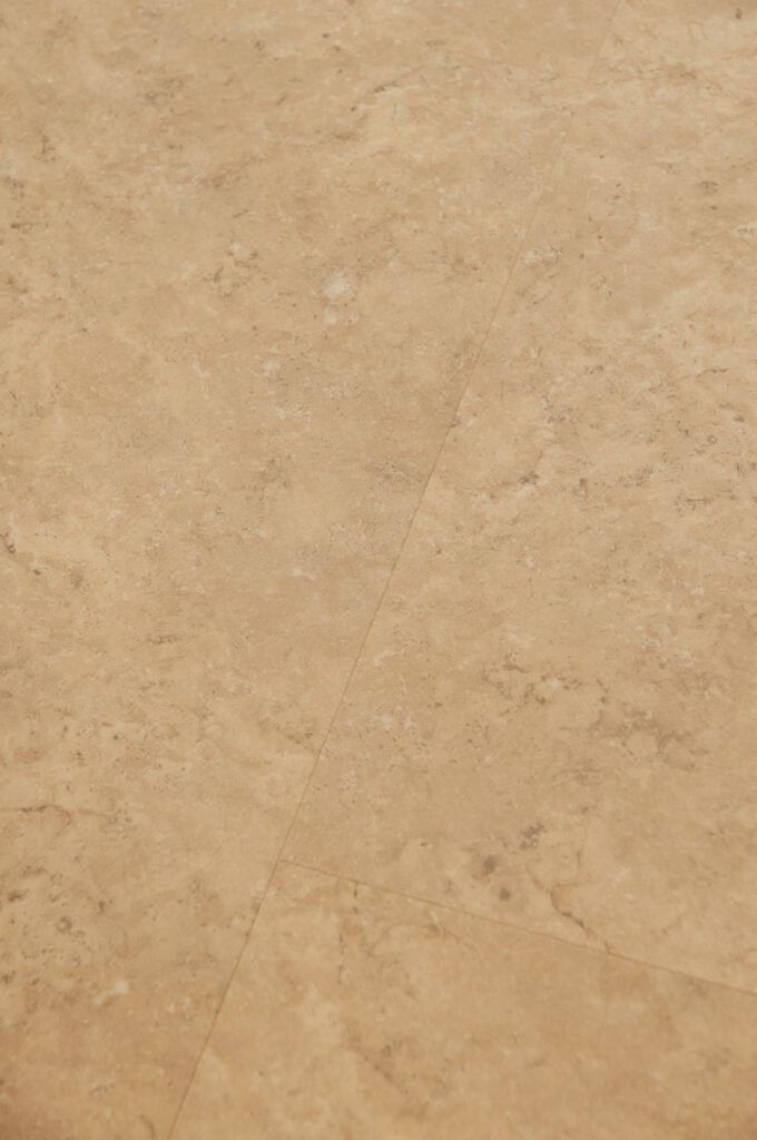 Close-up of a beige marble or stone tile floor with subtle veining and faint grout lines, creating a natural and textured appearance.
