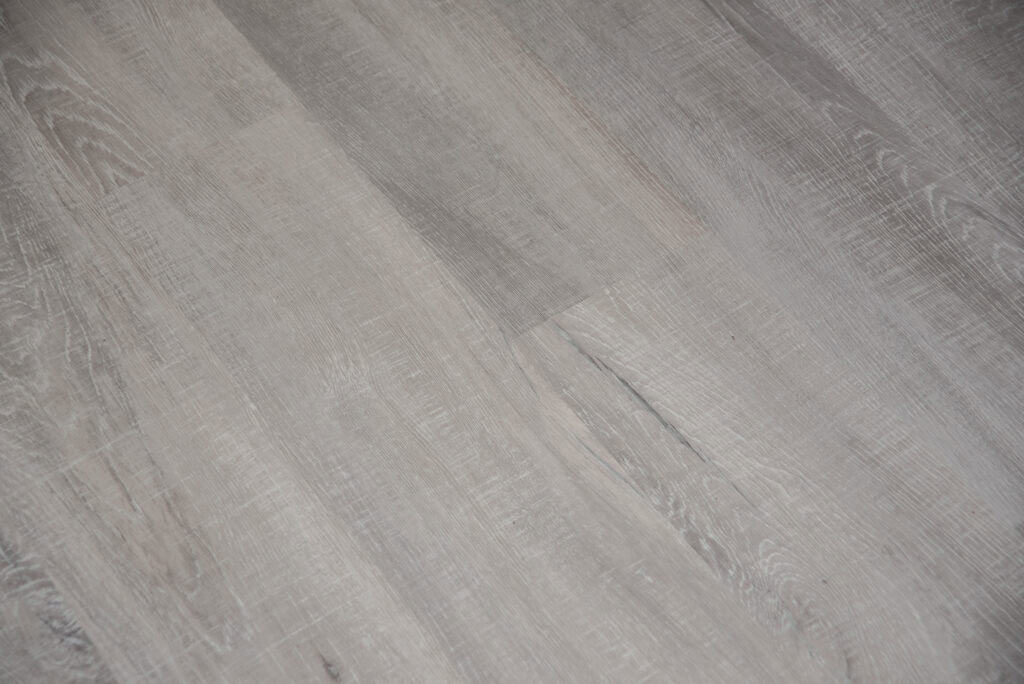 Close-up view of light grey wood flooring with a subtle grain texture and natural variations in color, showcasing the pattern and finish of the floor planks.