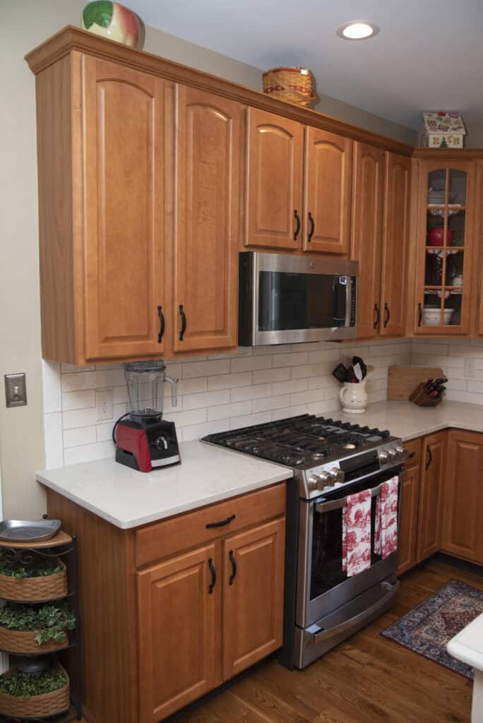 A kitchen corner with wooden cabinets, white countertops, a stainless steel stove and microwave, a red toaster, a blender, and kitchen towels hanging on the oven door.