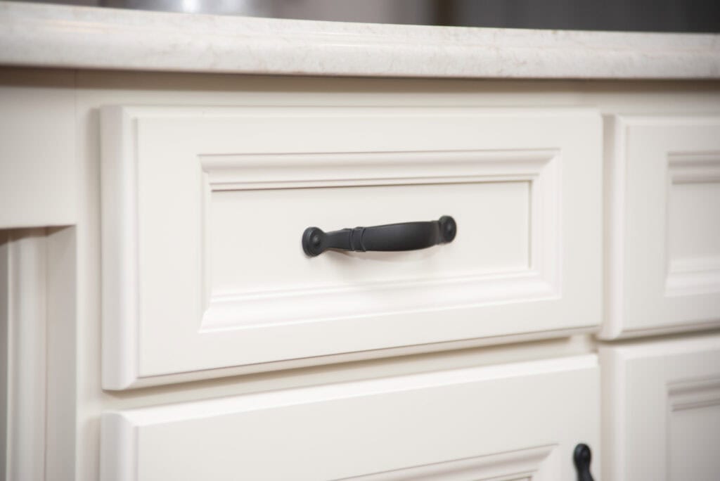 Close-up of an off-white cabinet drawer with a rectangular panel design and a black metal handle beneath a light-colored countertop.