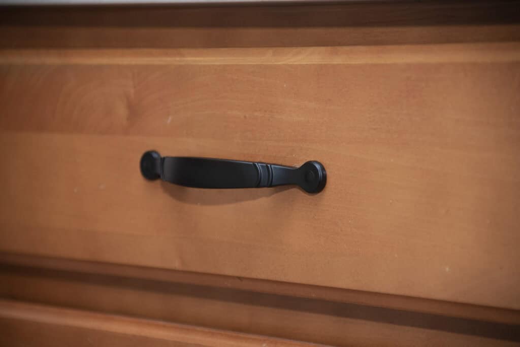 A close-up of a light brown wooden drawer with a black metal handle in the center.