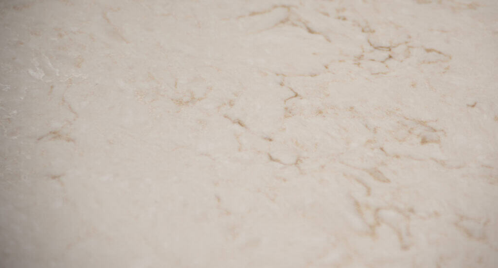 Close-up of a light beige marble surface with subtle, natural brown and tan veining patterns running across it. The texture appears smooth and slightly reflective.