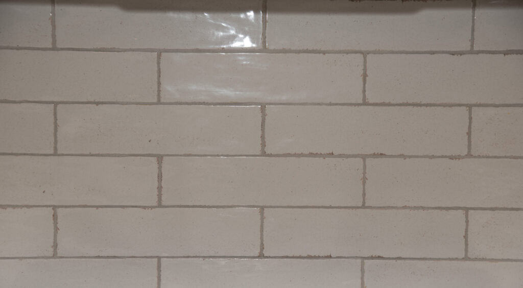 Beige rectangular subway tiles arranged in a horizontal brick pattern with slightly rough grout lines in between each tile.