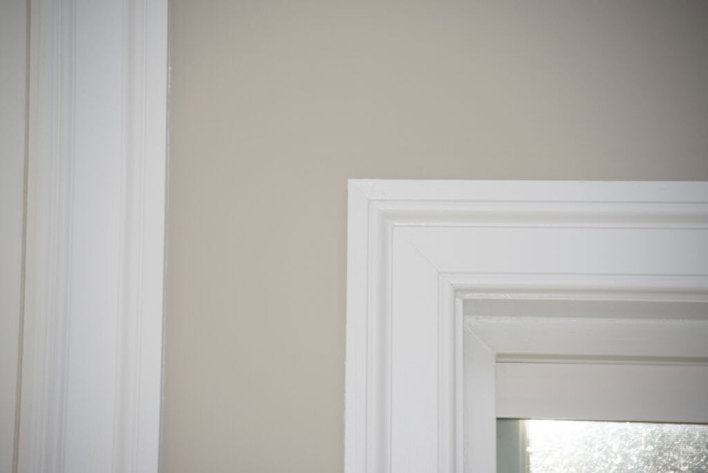 Close-up of the upper corner of a white door frame against a beige wall, with natural light coming through the window, highlighting the clean lines and molding details.