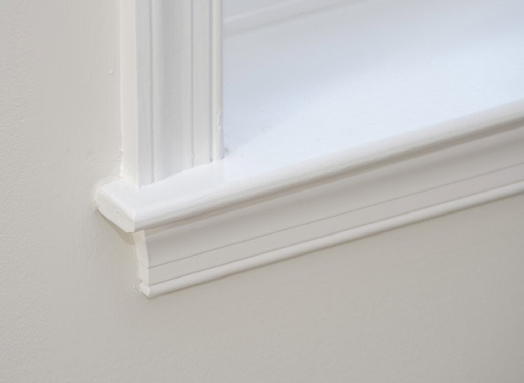 Close-up of a white painted window sill and trim, showing clean lines and smooth surfaces against a pale-colored wall.