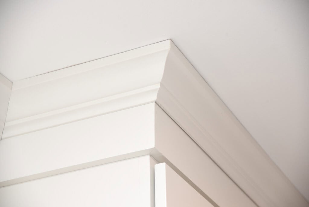 Close-up of white crown molding at the corner where a wall meets the ceiling, showing clean lines and smooth, angled trim detail.