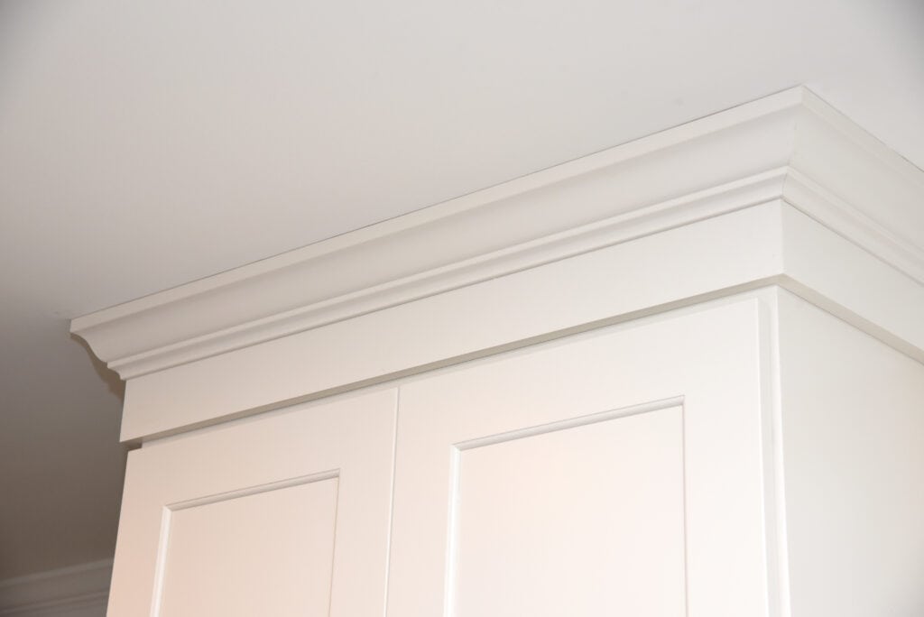Close-up of the top section of a white cabinet with crown molding, set against a plain white ceiling and wall.
