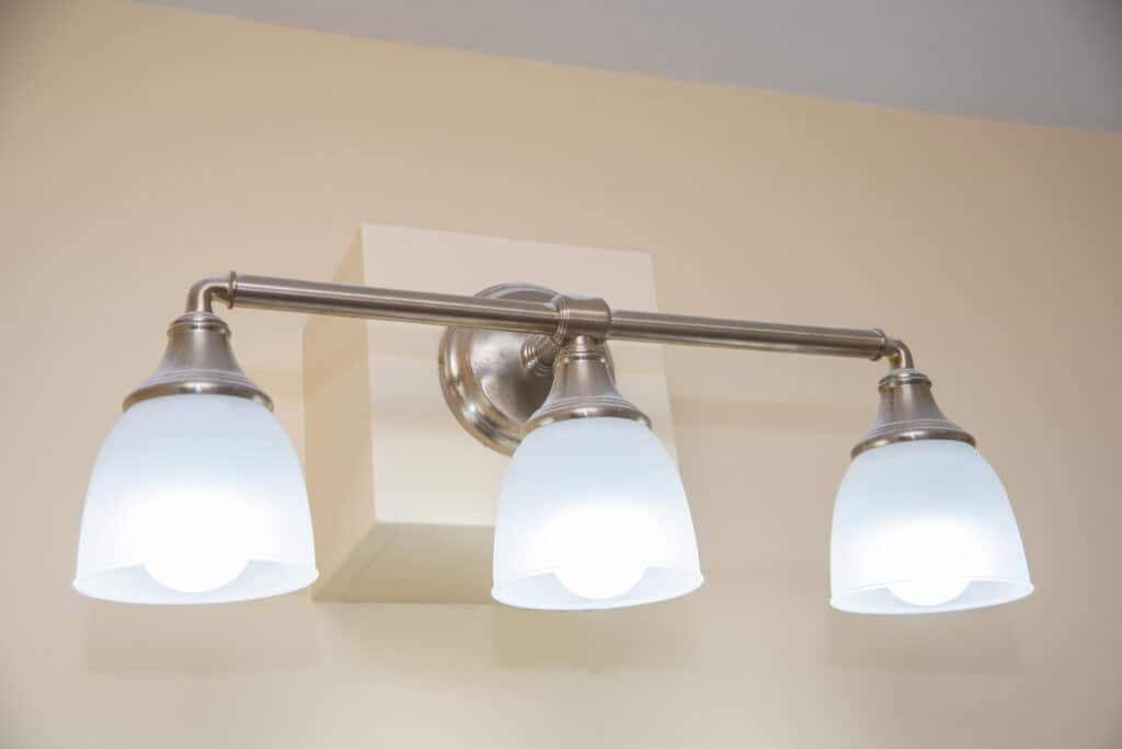 A brushed nickel three-light wall fixture with frosted glass shades is mounted on a beige wall, illuminating the space with soft, white light.