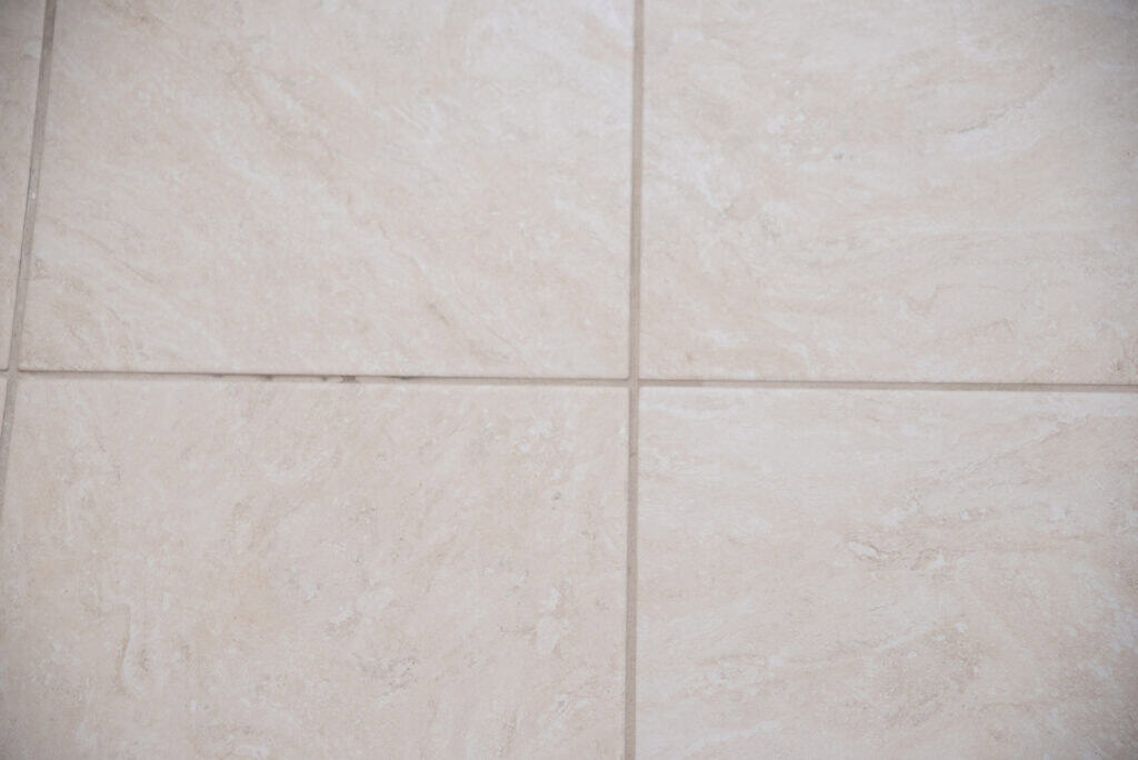 Close-up of four light beige ceramic floor tiles with subtle marbled patterns, separated by thin grout lines.