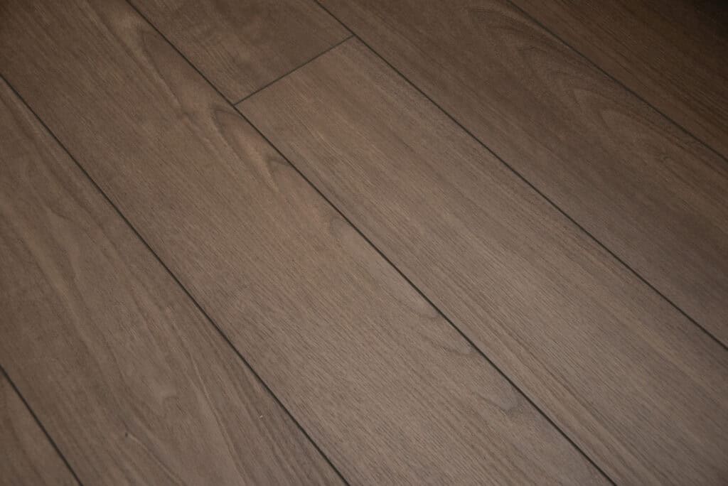 Close-up view of wooden floorboards with a smooth finish and natural wood grain patterns in a medium brown tone. The floorboards are aligned lengthwise and joined tightly together.