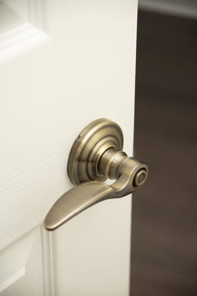 A brass door handle on a white door, partially open, with a dark, out-of-focus background.