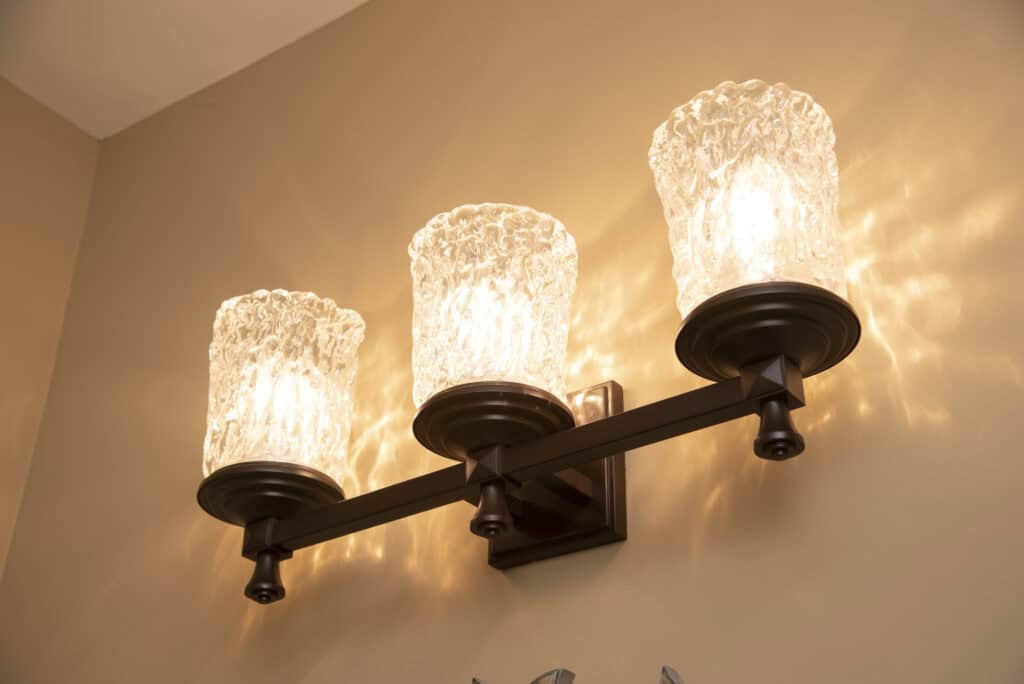 Three wall-mounted light fixtures with textured glass shades are illuminated, casting warm light and decorative patterns on a beige wall.