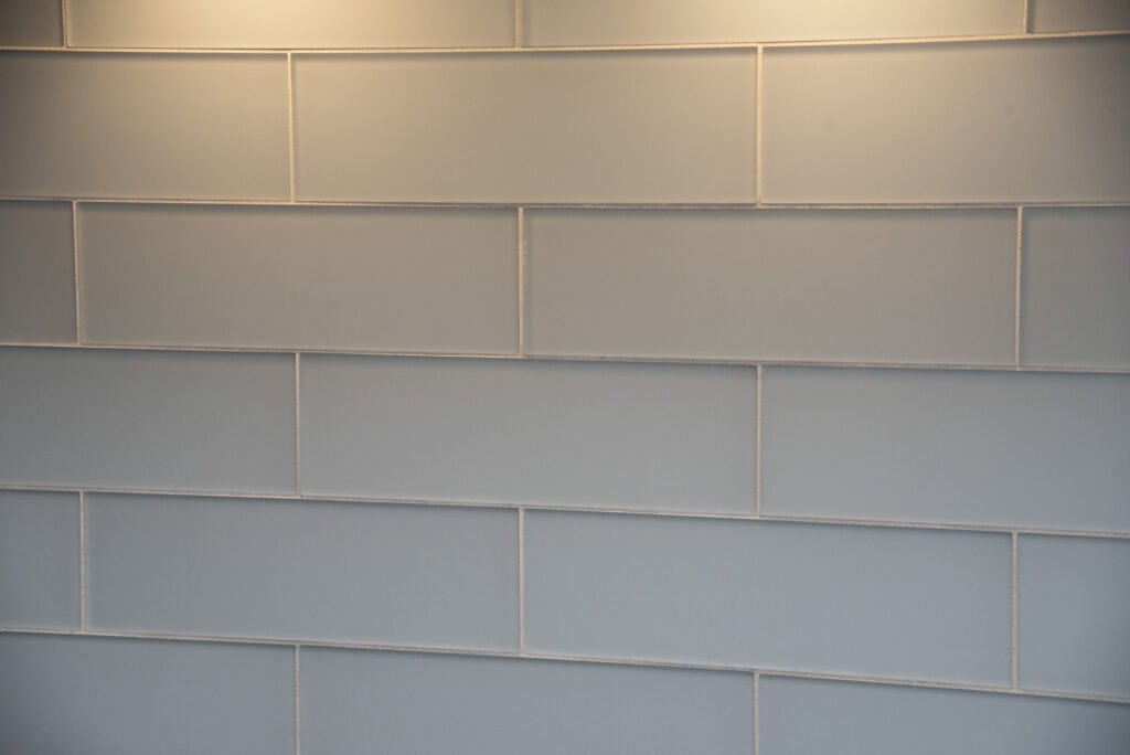 Light gray rectangular tiles arranged in a horizontal, staggered pattern on a wall with soft lighting from above.