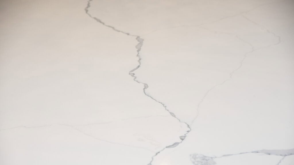 A close-up of a light-colored marble or stone surface with subtle gray veining and natural patterns running across it.