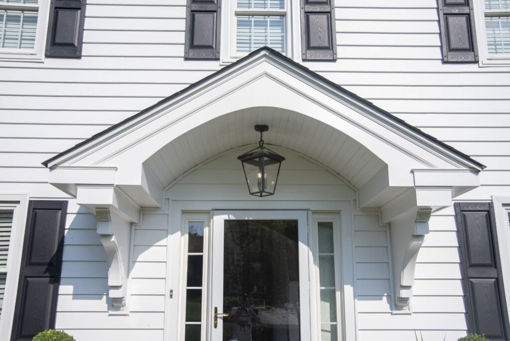 White house exterior with black shutters, arched entryway, glass front door, and a black lantern-style light fixture hanging above the entrance.