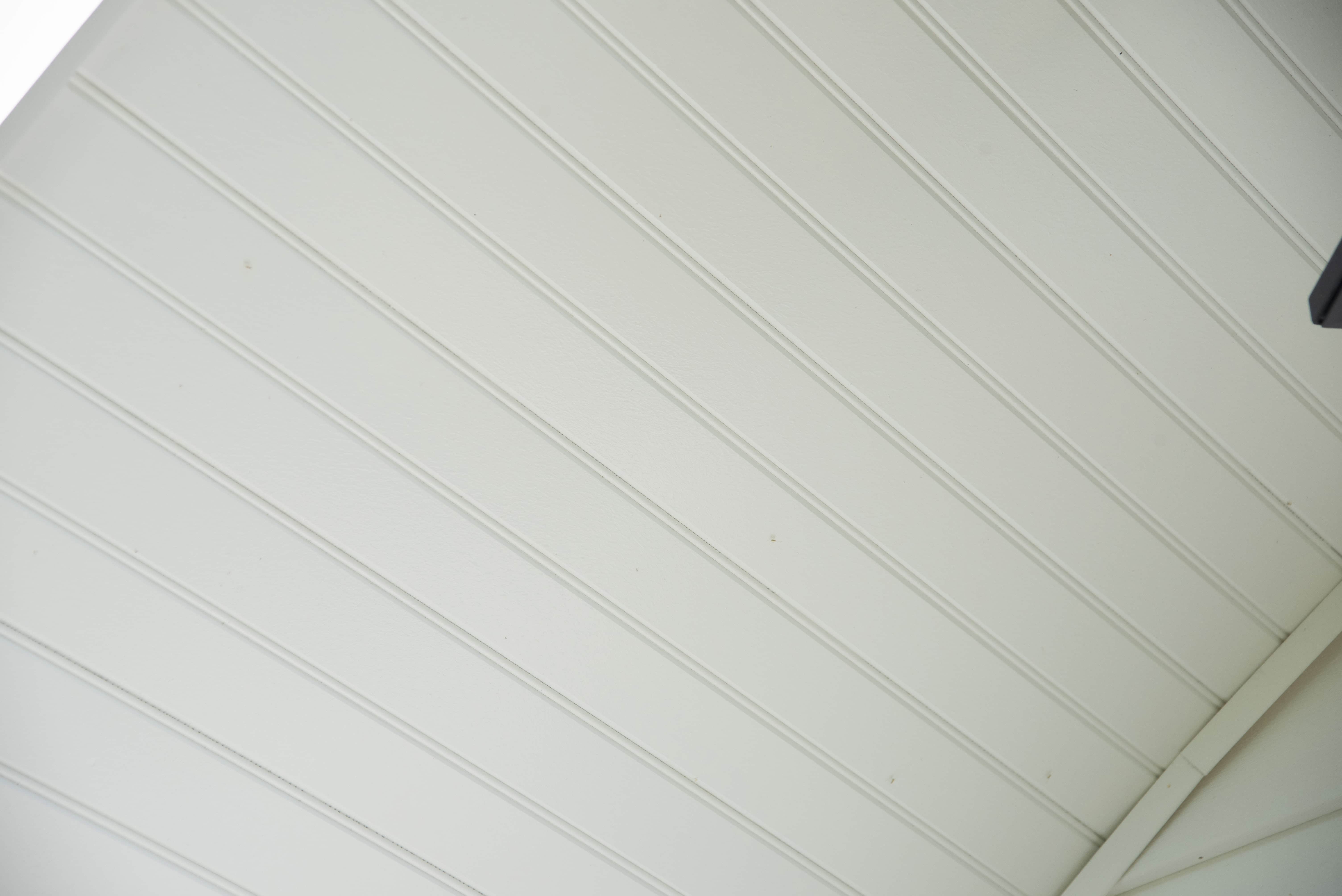 Close-up view of a white, paneled ceiling with evenly spaced vertical grooves and a portion of the ceilings edge visible in the corners.