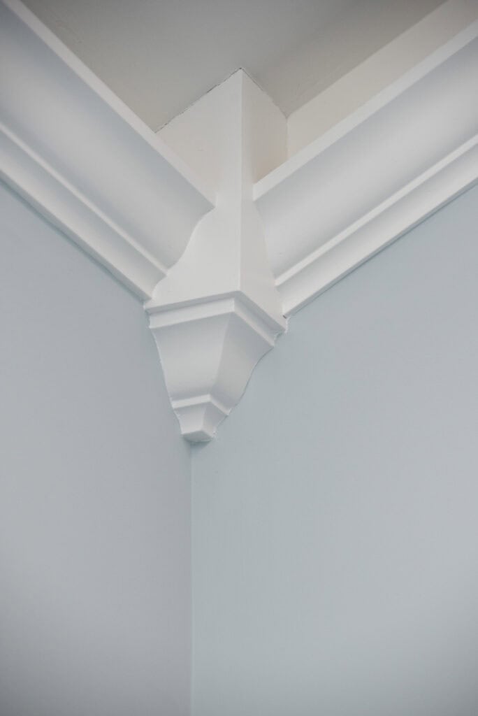 White decorative crown molding with an ornate corner block detail is installed at the intersection of two pale blue walls and the ceiling. The molding adds an elegant architectural accent to the room.