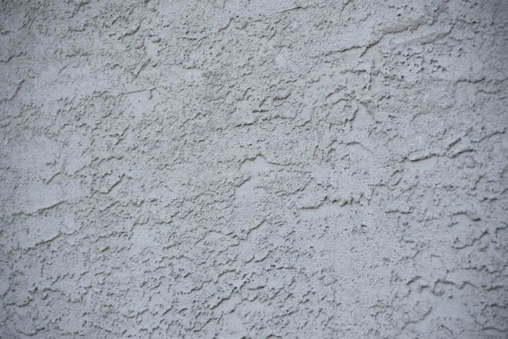 Close-up of a rough, light gray stucco wall with uneven, textured surface and irregular patterns.