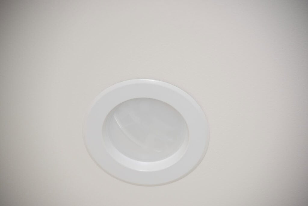 A close-up of a white recessed ceiling light fixture set in a plain, light-colored ceiling.