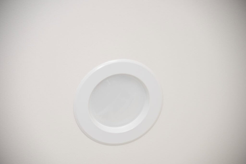 A round, white recessed ceiling light fixture is set into a plain, off-white ceiling.