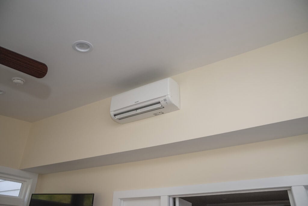 A white wall-mounted air conditioning unit is installed high on a beige wall above an open doorway in a modern room with white trim and a visible ceiling vent.