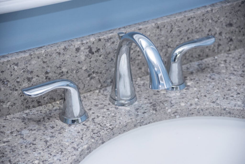 Chrome bathroom faucet with separate hot and cold handles mounted on a speckled gray granite countertop, next to a white sink and a blue wall in the background.