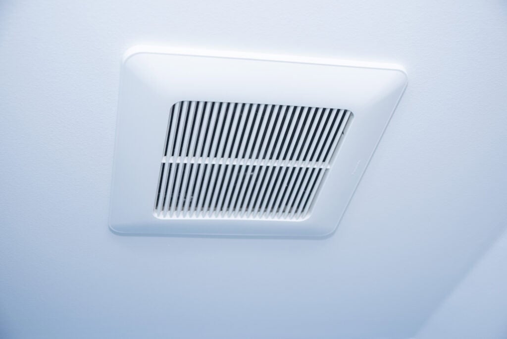 A white ceiling vent fan with horizontal slats, installed on a smooth, light blue ceiling.