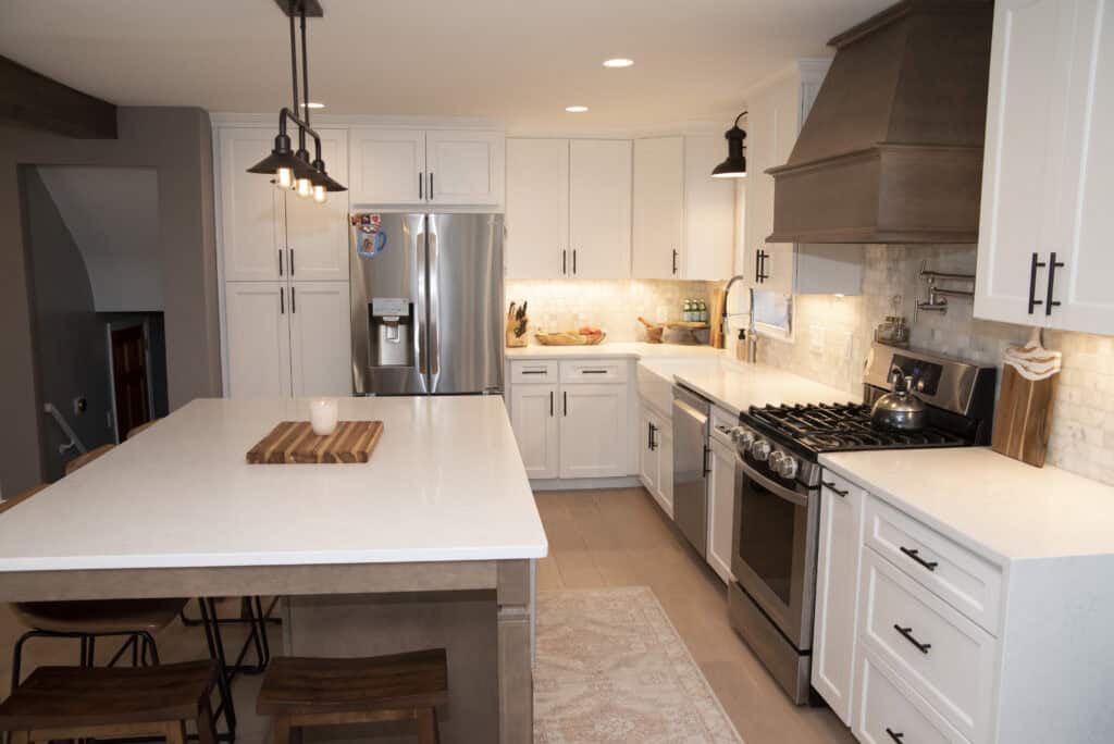 Modern kitchen with white cabinets, stainless steel appliances, a large island with wooden stools, a farmhouse sink, and a brown range hood. Warm lighting and neutral tones create a cozy, inviting atmosphere.