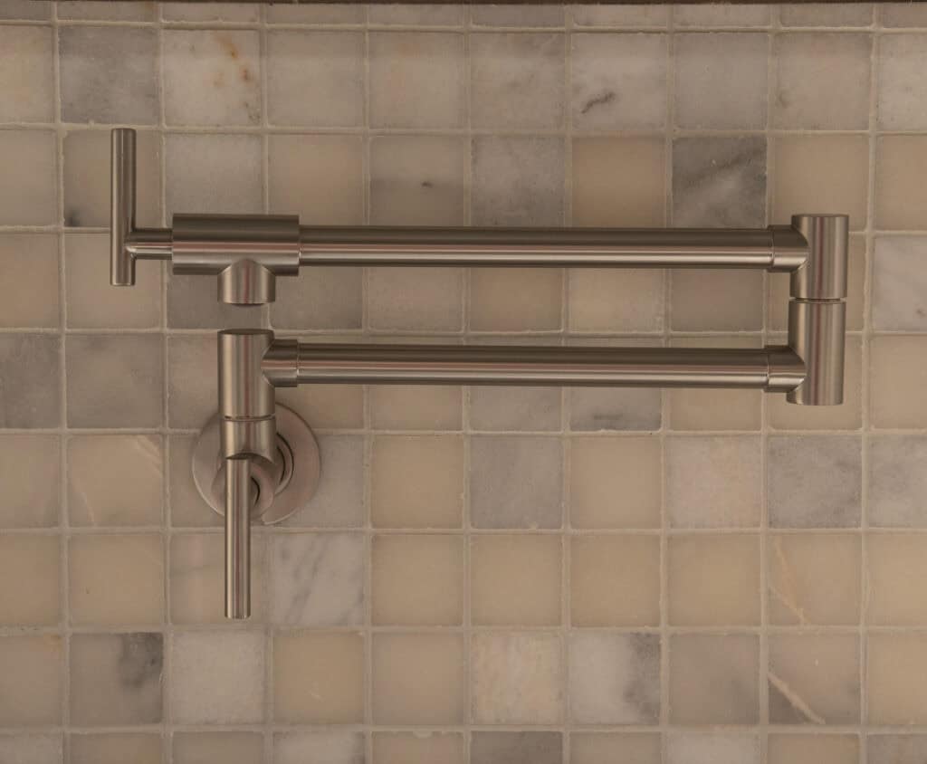 Two brushed metal, jointed pot filler arms mounted on a beige and light brown tiled backsplash wall, shown folded flat against the surface.