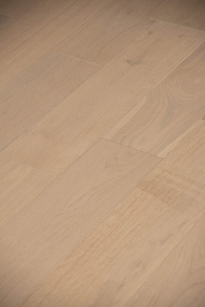 Close-up of light-colored wooden floorboards with visible grain patterns and seams between the planks. The surface appears smooth and clean, reflecting a soft, natural finish.