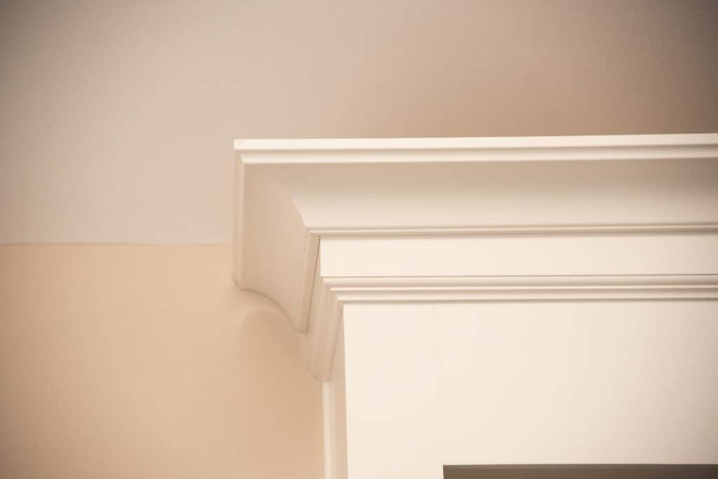 Close-up of white crown molding at the top corner of a wall, showing the detailed trim work where the ceiling and two walls meet.