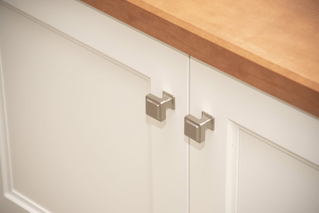 Close-up of white cabinet doors with modern square silver handles and a light wood countertop above.